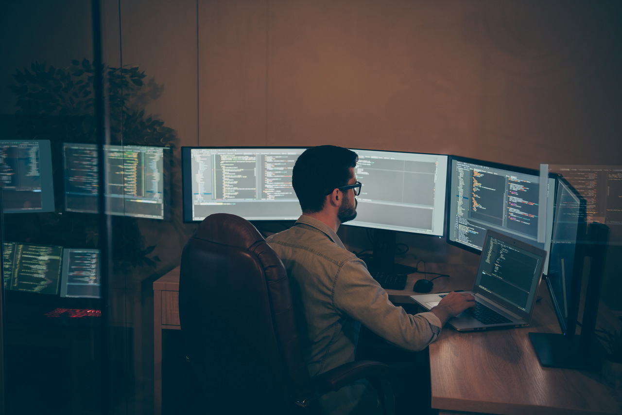 programista podczas pracy, mężczyzna siedzący przy kilku monitorach