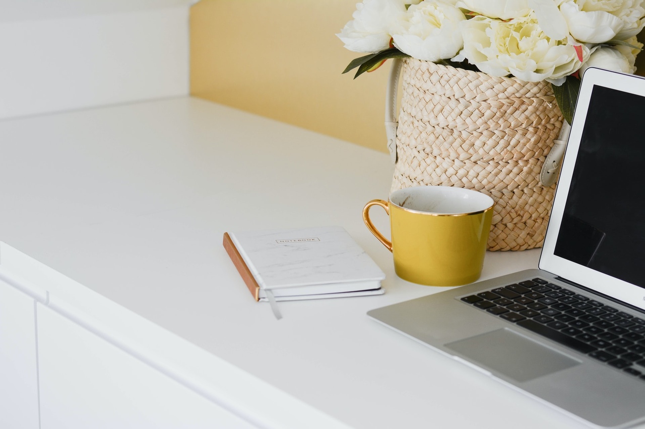 laptop lezacy na biurku wraz z notatnikiem, obok stoi kawa w kubku