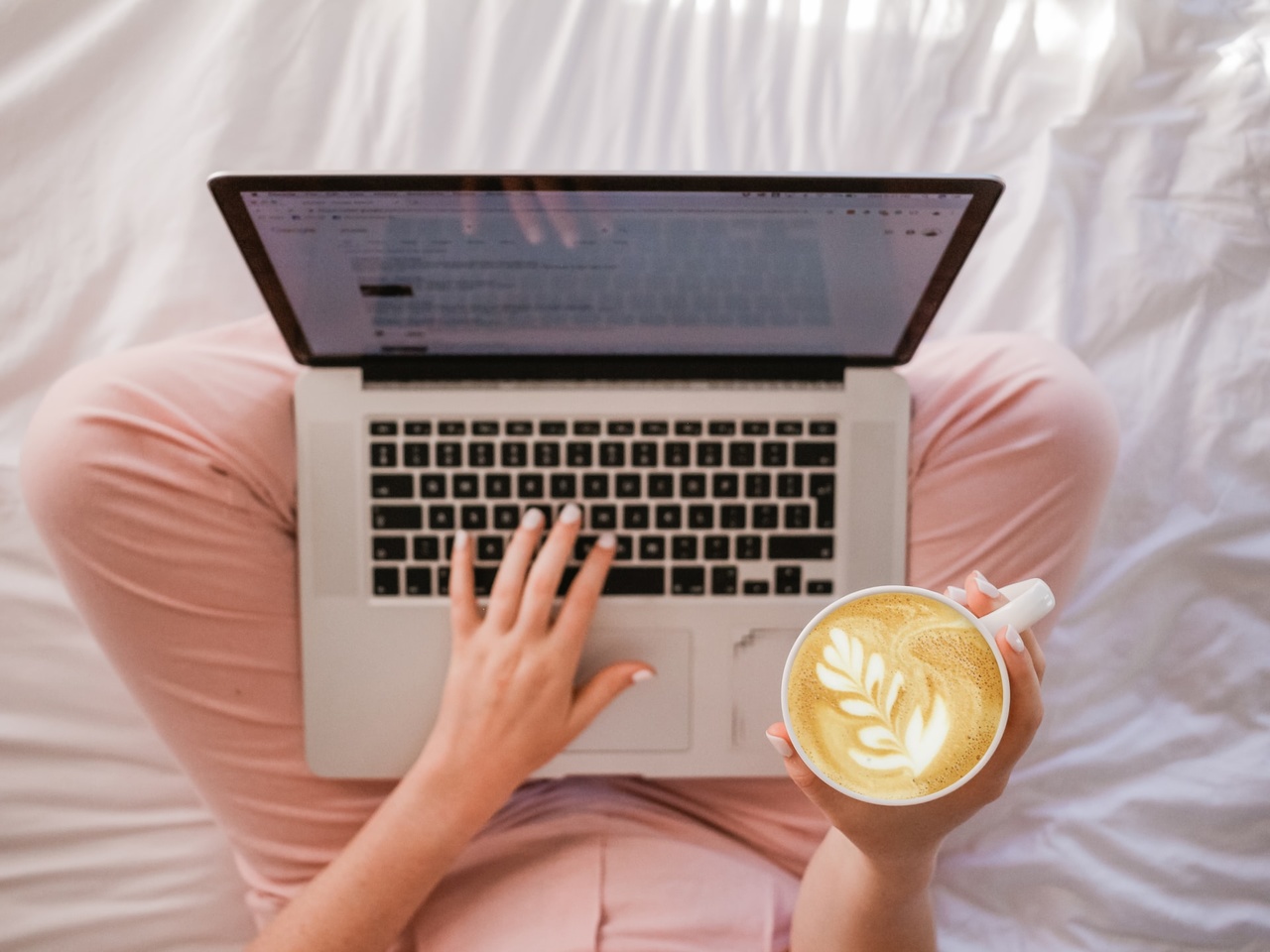 jak pozycjonowac bloga, kobieta siedzaca na lozku z laptopem na nogach, w dloni trzymajaca kawe