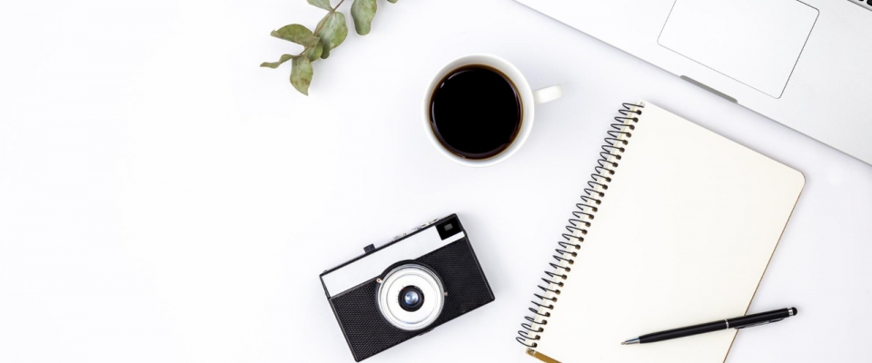 aparat leżący na stole, obok notatnik i długopis, kawa i laptop, skąd brać zdjęcia na bloga